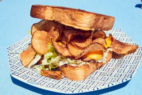 A stacked sandwich with lettuce and cheese, topped with crispy potato chips, served on a decorative plate.