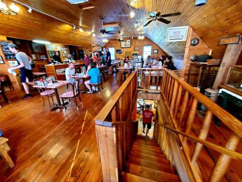 A cozy restaurant interior with wooden decor, tables filled with diners, and a staircase leading to a lower level.
