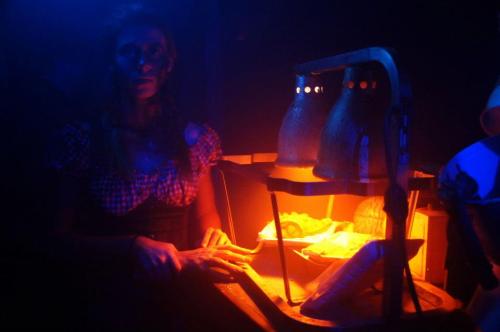 A dimly lit scene featuring a woman in a checkered outfit, illuminated by orange light from lamps.