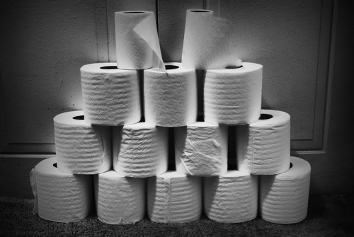 A pyramid of white toilet paper rolls stacked against a wall, with varying heights and textures.