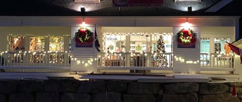 A festive building decorated with holiday lights and wreaths, featuring a Christmas tree visible inside.