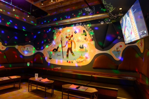 A colorful karaoke room with a mural, seating, and disco lights reflecting on the walls.