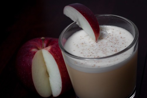 A glass of creamy beverage topped with a slice of red apple, next to a whole red apple cut in half.