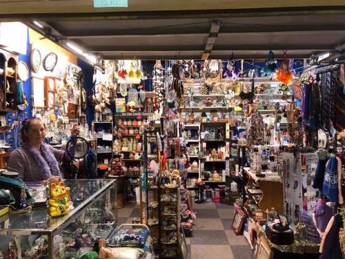 A vibrant shop filled with various trinkets, decorations, and collectibles, with a woman standing by the display counter.