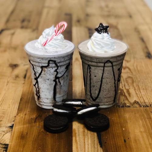 Two festive milkshakes topped with whipped cream, one with a candy cane and the other with a star, beside Oreo cookies.