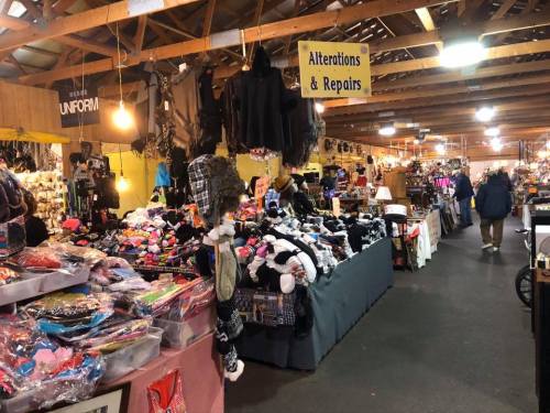 A bustling market scene with various stalls selling clothing, accessories, and a sign for alterations and repairs.