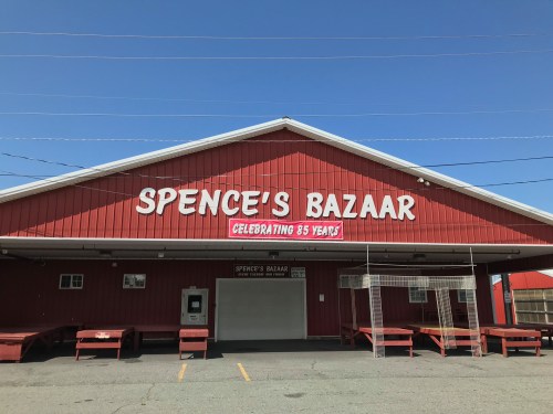 Red building with "Spence's Bazaar" sign and "Celebrating 85 Years" banner under a clear blue sky.