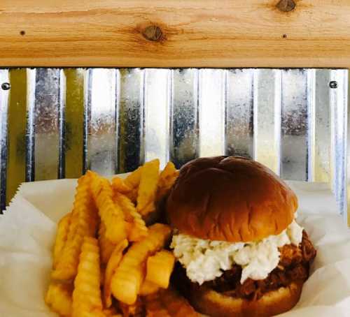 A crispy chicken sandwich topped with creamy sauce, served with a side of golden crinkle-cut fries.