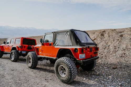 Two off-road vehicles parked on a rocky terrain, with mountains in the background and a clear sky above.