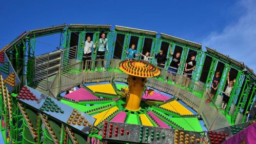 A colorful amusement park ride with people standing on it, surrounded by vibrant lights and a clear blue sky.