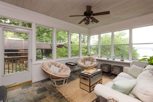 Bright sunroom with large windows, cozy seating, a coffee table, and a view of greenery outside.