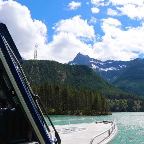 A boat on a calm lake with lush green mountains and snow-capped peaks under a partly cloudy sky.