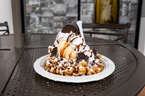 A dessert plate featuring a mountain of funnel cake topped with ice cream, whipped cream, chocolate sauce, and Oreos.