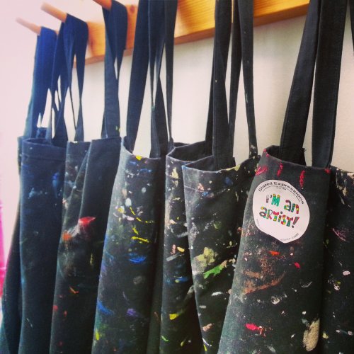 A row of colorful, paint-splattered aprons hanging on a wall, with one featuring a badge that says "I'm an artist!"