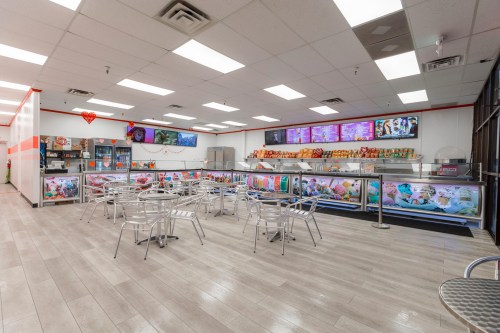 Bright ice cream shop interior with colorful displays, seating area, and a menu board on the wall.