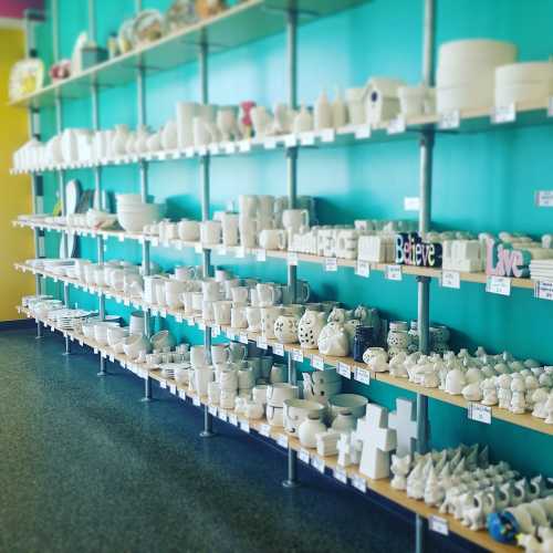 A colorful wall displays shelves filled with various white ceramic items, including mugs, figurines, and decorative pieces.