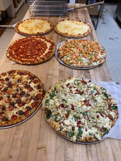 A variety of pizzas on wooden tables, including pepperoni, cheese, veggie, and specialty toppings.