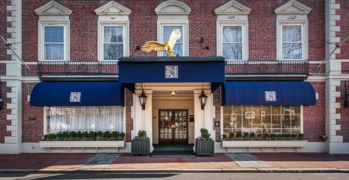A brick building with a blue awning and a golden eagle statue on top, featuring large windows and potted plants.