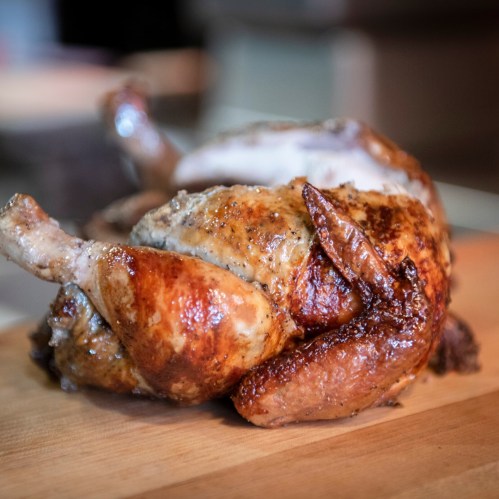 A perfectly roasted chicken on a wooden cutting board, showcasing golden-brown skin and crispy wings.