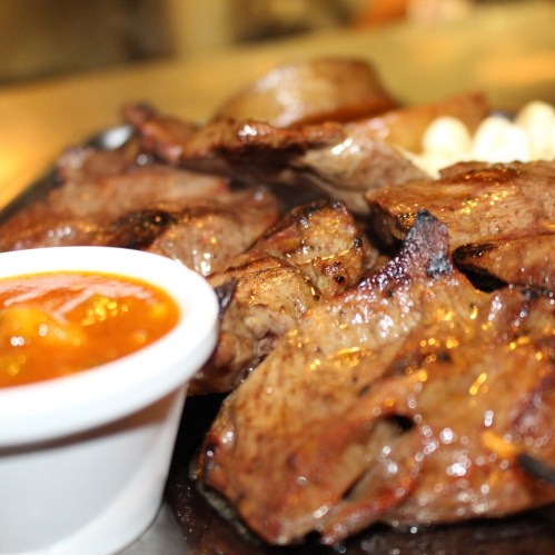 Grilled meat served with a side of dipping sauce on a plate.