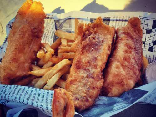 A serving of crispy fried fish fillets with golden French fries, presented in a paper-lined basket.