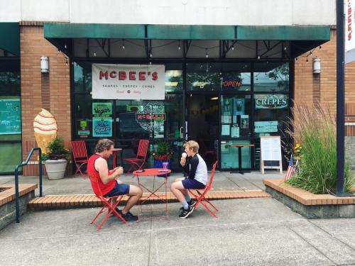 Two people sit at red bistro tables outside McBee's, a casual eatery, enjoying food in a vibrant, welcoming atmosphere.