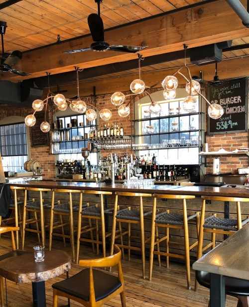 A cozy bar with wooden accents, hanging light fixtures, and a well-stocked shelf of drinks in a warm, inviting atmosphere.