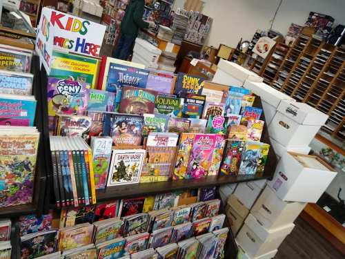 A colorful display of comic books and graphic novels in a bookstore, with boxes and shelves in the background.