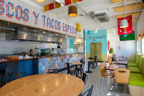 Bright, colorful taco restaurant interior with a counter, tables, and a welcoming atmosphere.