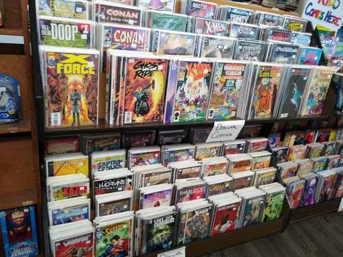 A display of comic books on shelves, featuring titles like X-Force, Conan, and Ghost Rider.