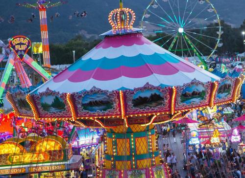 A vibrant carnival scene featuring colorful rides, lights, and crowds enjoying the festivities at dusk.