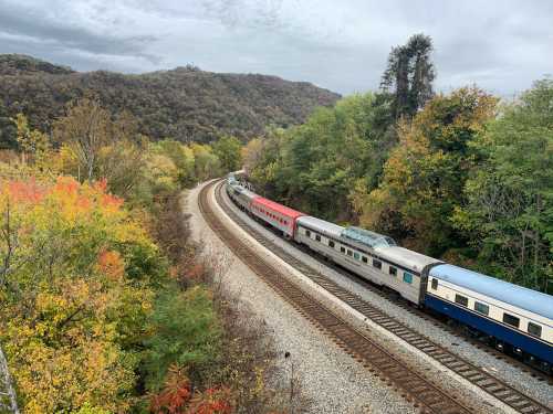 A train travels along a curved track surrounded by colorful autumn foliage and rolling hills.