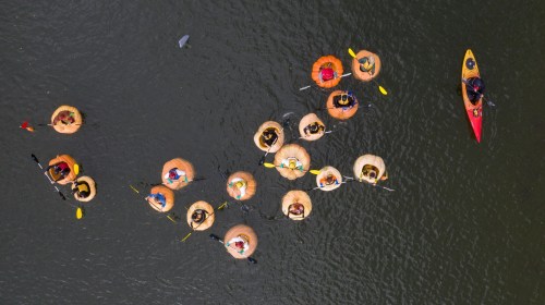 Aerial view of people in colorful inflatable rafts and kayaks on a calm water surface.