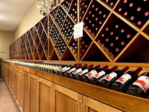 A wooden wine rack filled with various bottles of wine, neatly organized in a well-lit room.