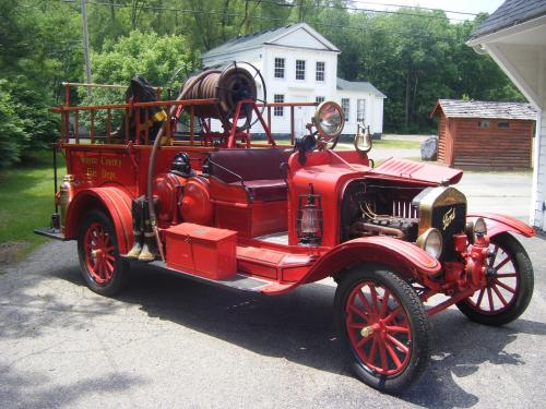 A vintage red fire truck parked outside a building, featuring a hose reel and classic design elements.