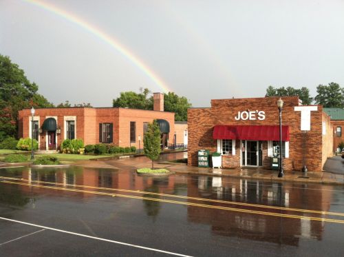 A brick building with a red awning labeled "Joe's" on a rainy day, with a rainbow in the background.