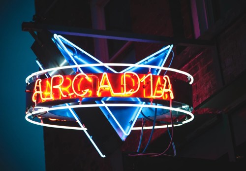 Neon sign for "Arcadia" with a star shape, glowing in vibrant blue and red against a dark background.