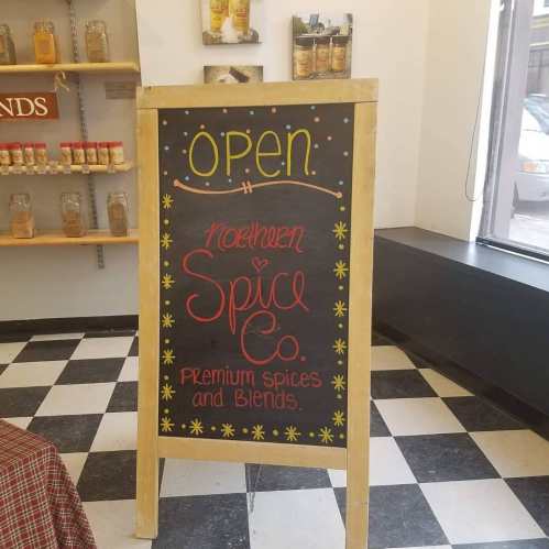 A chalkboard sign reads "Open" and "Meadowen Spice Co. Premium Spices & Blends" in a shop with spice jars in the background.