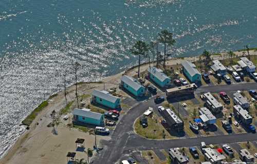 Aerial view of a waterfront area with several houses and RVs along a winding road by the water's edge.