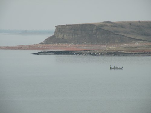 A small boat on calm water near a rocky cliff under a hazy sky.