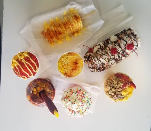 A variety of colorful desserts including ice cream, fruit cups, and sweet toppings arranged on a white surface.
