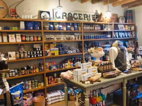A cozy grocery store interior with shelves filled with various food products and a display table in the foreground.
