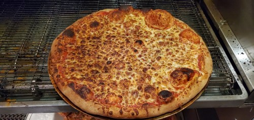 A large, freshly baked pizza with melted cheese and pepperoni, resting on a cooling rack.