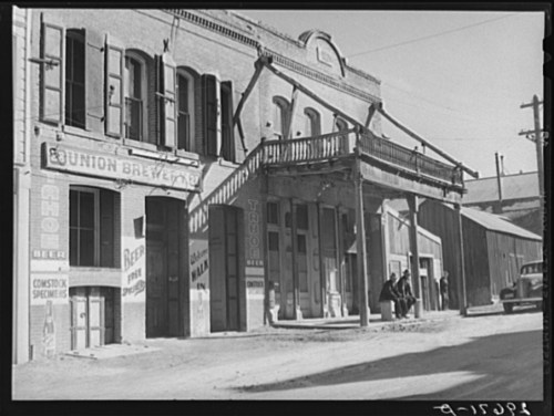 Historic street view featuring the Bunion Brewery, wooden balcony, and vintage cars parked outside.