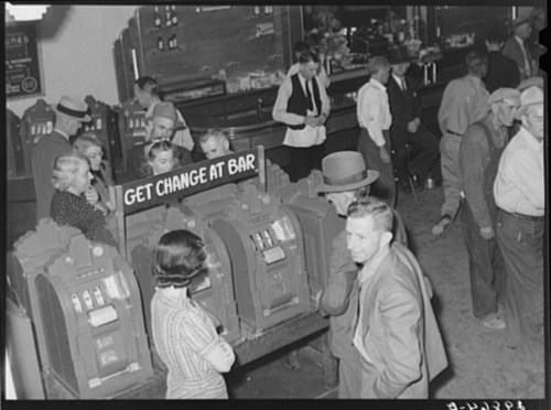 A vintage bar scene with patrons near slot machines, a sign reading "GET CHANGE AT BAR" visible in the foreground.