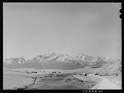 A panoramic view of a mountainous landscape with a small settlement in the foreground under a clear sky.