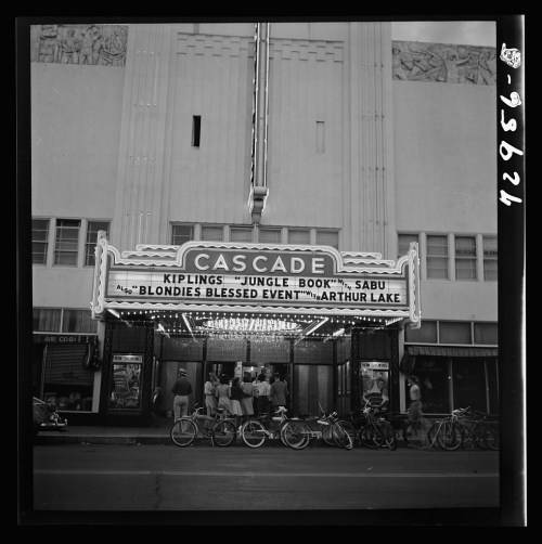 Historic theater marquee displaying "Cascade" with movie titles and a crowd outside, surrounded by bicycles.