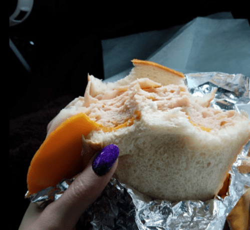A hand holding a sandwich with turkey and cheese, partially eaten, wrapped in foil.