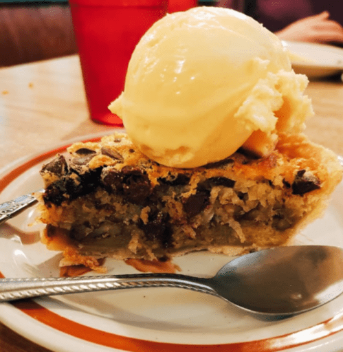 A slice of pie topped with a scoop of vanilla ice cream on a plate, with a spoon beside it.