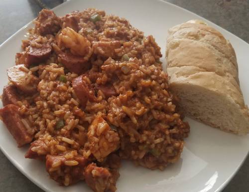 A plate of flavorful rice with shrimp and sausage, accompanied by a slice of fresh bread.